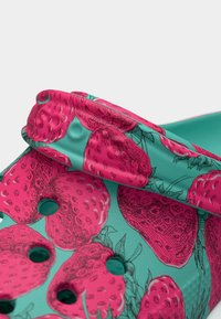 Κοντινό πλάνο πράσινου τσόκαρου με ροζ σχέδιο φράουλας και οπές αερισμού στις επάνω και πλαϊνές λουρίδες.