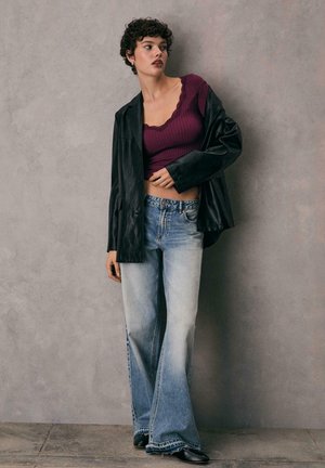 Blazer oversize in pelle nera, top corto a coste borgogna con pizzo, jeans svasati azzurri, scarpe nere, texture liscia.