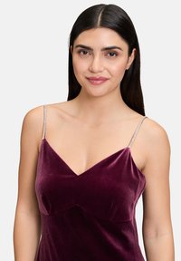 Robe en velours bordeaux avec un décolleté en V et de fines bretelles ornées ; texture lisse avec des détails de cintrage subtils sur le corsage.