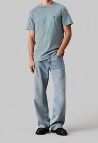 Vaaleansininen puuvillainen lyhythihainen T-paita, jossa on pyöreä pääntie, yhdistetty löysään, haalistuneisiin sinisiin farkkuihin ja mustiin nahkakenkiin.