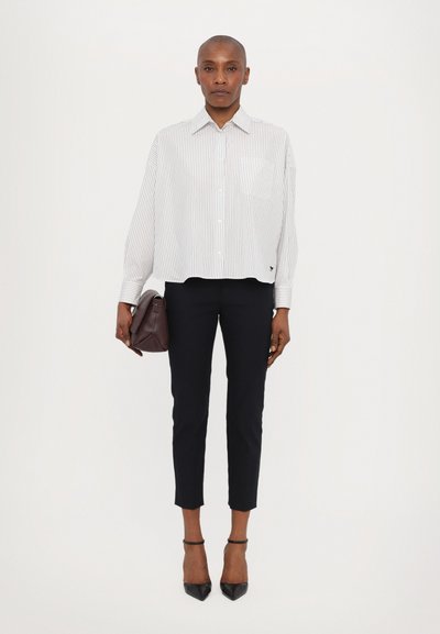 Gestreept wit en grijs cropped shirt met knoopsluiting, gecombineerd met zwarte broek tot de enkel en zwarte hakken, met een kleine bordeauxrode tas.