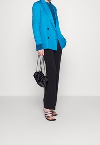Jasnoniebieska marynarka dwurzędowa na teksturowanym turkusowym topie, zestawiona z czarnymi szerokimi spodniami, czarną marszczoną torebką i sandałami na paski.