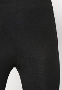Leggings pretos feitos de tecido texturizado com um brilho subtil, apresentando um ajuste confortável e cintura elástica.