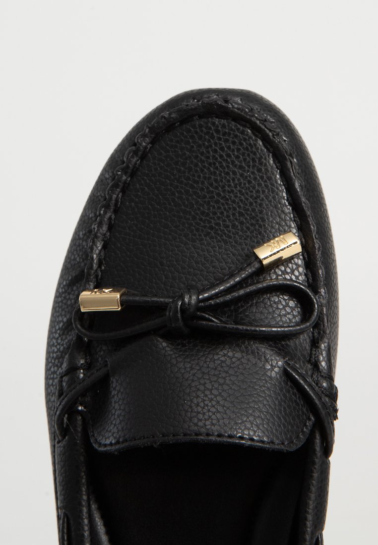 Mocassino in pelle nera con finitura testurizzata, punta tondeggiante e un fiocco decorativo con dettagli in metallo dorato.