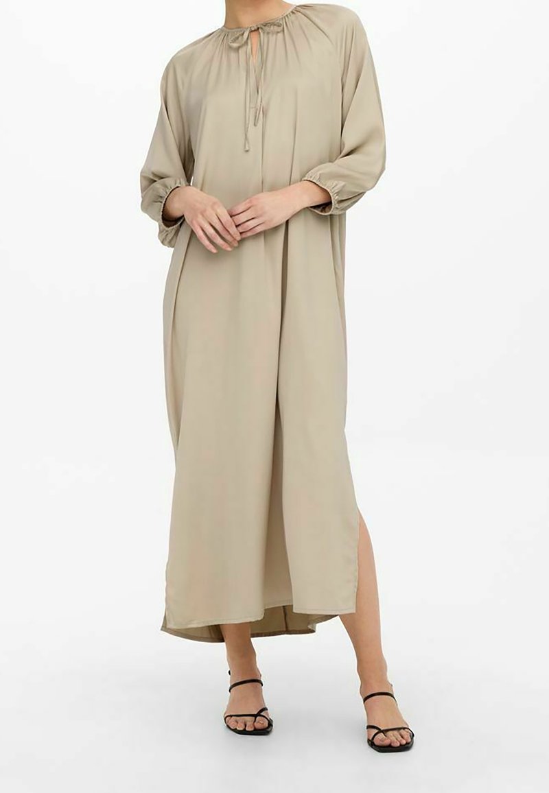 Vestido maxi beige con cuello fruncido, cordón de ajuste y mangas largas. Cuenta con una abertura lateral y una tela suave y ligera.