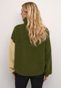 Pullover in pile verde e crema con colletto alto, motivo testurizzato, vestibilità svasata e polsini a coste. La vista posteriore mostra un design a blocchi di colore contrastante.