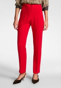 Pantaloni su misura rossi con una texture liscia, vita alta e pieghe, dotati di chiusura a bottone e design a gamba affusolata.