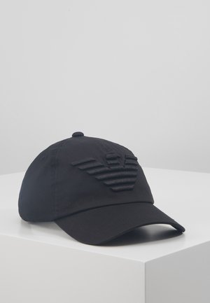 Black cotton cap with a structured peak, featuring a textured emblem resembling wings on the front. Simple, sleek design.