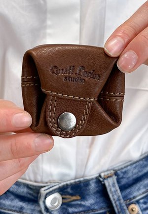 Braune Ledertasche mit Druckknopfverschluss, ausgestattet mit cremefarbenen Nähten und geprägtem Logo. Kompakte Bauweise, weiche Textur.