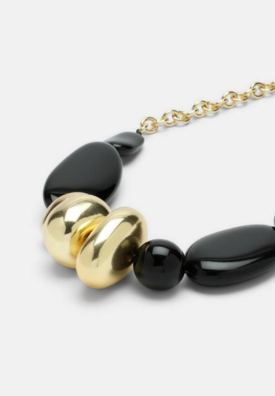 Collier perlé en or et noir avec des formes ovales et rondes noires brillantes, incluant un disque central en or, fixé par une chaîne.