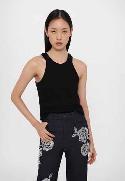 Zwarte geribbelde mouwloze top met een ronde halslijn, gecombineerd met donkerdenim broek met witte bloemenborduursels op de benen.