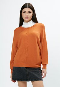 Oranger Strickpullover mit Rundhalsausschnitt, Kabelstrick-Details in der Mitte und gerippten Bündchen, kombiniert mit einem schwarzen Denim-Minirock.