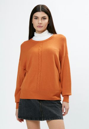 Oranje gebreide trui met een ronde hals, kabelbreipatroon in het midden en geribbelde mouwen, gecombineerd met een zwarte denim minirok.
