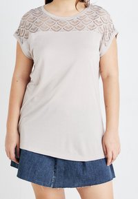 Ljusbeige t-shirt med kort ärm och ett mönstrat spetsöverdel, kombinerad med en mörk denimkjol. Mjuk textur. Avslappnad passform.