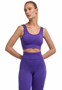 Fioletowy sportowy biustonosz z okrągłym dekoltem i krótkim krojem, połączony z legginsami z wysokim stanem zdobionymi teksturowanymi wzorami w zygzak.