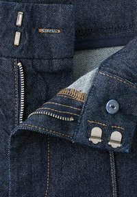 Temno modra denim tkanina z vidno teksturo, s srebrno kovino, kontrastnim šivom, zadrgo in gumbi na pasu.