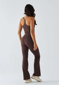 Brązowy strój sportowy składający się z dopasowanego topu i rozkloszowanych spodni, wykonany z elastycznego materiału, z cienkimi ramiączkami i bezszwową konstrukcją.