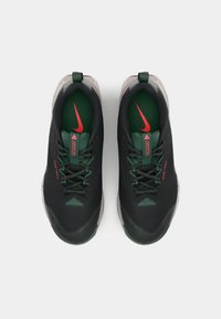 Chaussures de sport noires avec des accents verts et rouges, présentant une tige en tissu texturé, un système de laçage et un talon renforcé pour le soutien.