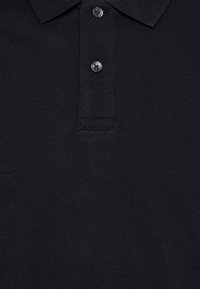 Polo shirt nera realizzata in tessuto testurizzato, con colletto classico, tre bottoni e un dettaglio di placca discreta.