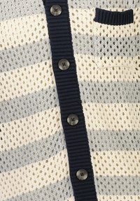 Stickad cardigan med lös och öppen väv i grått och krämfärgade ränder. Har en marinblå knappslå och en liten marinblå fickdetalj.