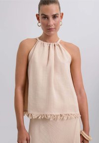 Top halter beige claro con escote fruncido y detalle de flecos en el dobladillo, hecho de una tela texturizada. Diseño sencillo, sin mangas.