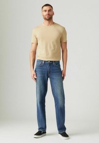 Camiseta de cuello redondo beige, combinada con jeans de mezclilla azul de pierna recta. Los jeans cuentan con un diseño clásico de cinco bolsillos y un sutil desgastado.
