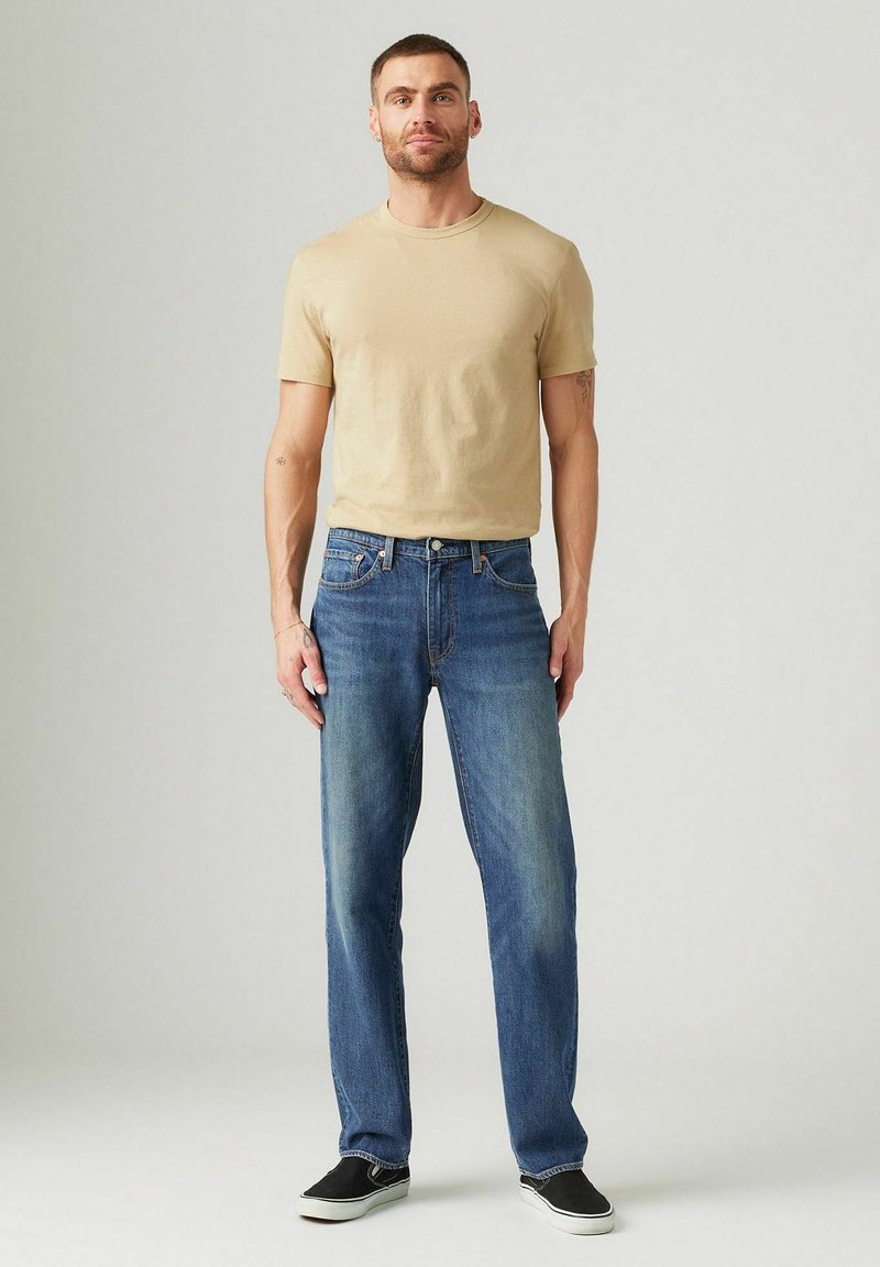 Camiseta de cuello redondo beige, combinada con jeans de mezclilla azul de pierna recta. Los jeans cuentan con un diseño clásico de cinco bolsillos y un sutil desgastado.