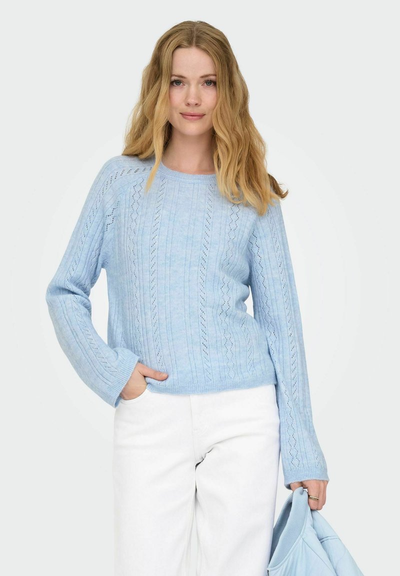 Pull en tricot bleu clair avec un motif texturé, manches longues et encolure ronde, assorti à un pantalon blanc.