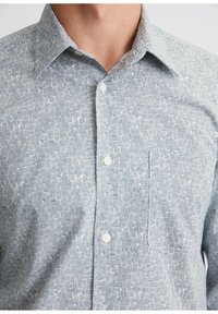 Light blue button-up shirt with a textured pattern of vertical and horizontal lines. Features classic collar and a chest pocket.