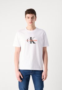 Hvit bomull T-skjorte med et frontlogo som sier "Calvin Klein Jeans" i oransje og grått, parret med blå denimjeans.