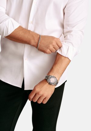 Silver stainless steel watch with a textured gray dial and silver bracelet. White button-up shirt. Black pants with rolled sleeves.
