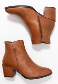 Ruskeat nahkaiset nilkkurit, joissa on terävä kärkiosa, sivuvetoketju ja paksu korko. Sileä pinta, ei kuvioita tai lisäkoristeita.