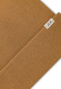 Beanie marrone lavorato a maglia in filato spesso, con un'etichetta con il logo. La textura è a coste con una finitura liscia.