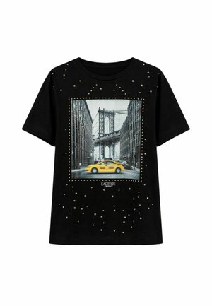 Camicia nera a maniche corte con borchie e una foto cittadina di un taxi giallo che passa sotto un ponte urbano tra alti edifici.