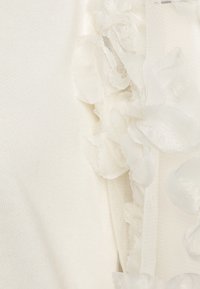 Abito bianco con rouches testurizzati realizzati in tessuto trasparente su un lato, su uno sfondo liscio e uniforme di colore bianco.