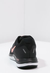 Black athletic sneaker with a textured upper, pink Nike logo, reflective accents, and a white midsole. View from the rear.
