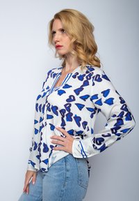 Koszula zapinana na guziki o białej bazie, z niebieskim wzorem serc oraz niebieskimi paskami przy dekolcie i mankietach. Długie rękawy.