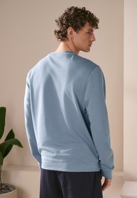Lichtblauwe longsleeve sweat met ronde hals, zachte textuur en geribbelde manchetten, van achteren getoond tegen een neutrale achtergrond.