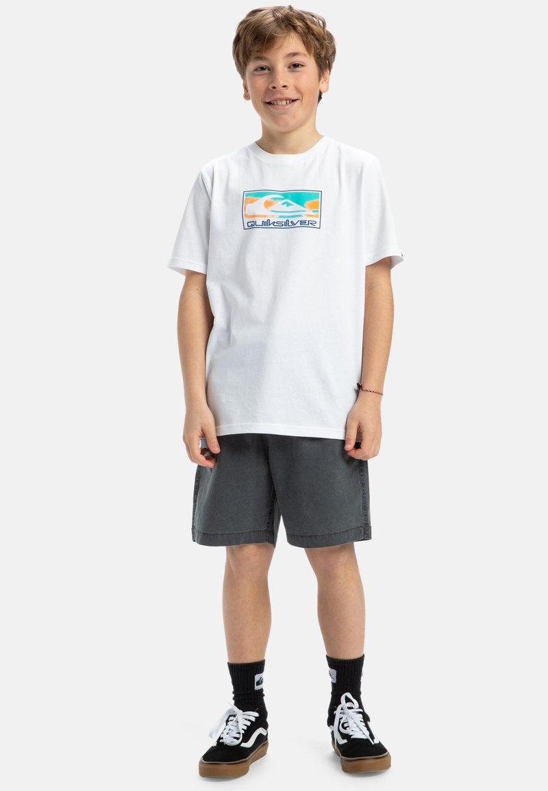 Vit bomull t-shirt med en flerfärgad grafik och "Quiksilver"-logotyp, tillsammans med grå shorts och svarta sneakers.