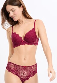 Bordowy koronkowy biustonosz z wkładkami i regulowanymi ramiączkami; dopasowane koronkowe majtki z falbankowymi krawędziami i małą kokardką na środku.