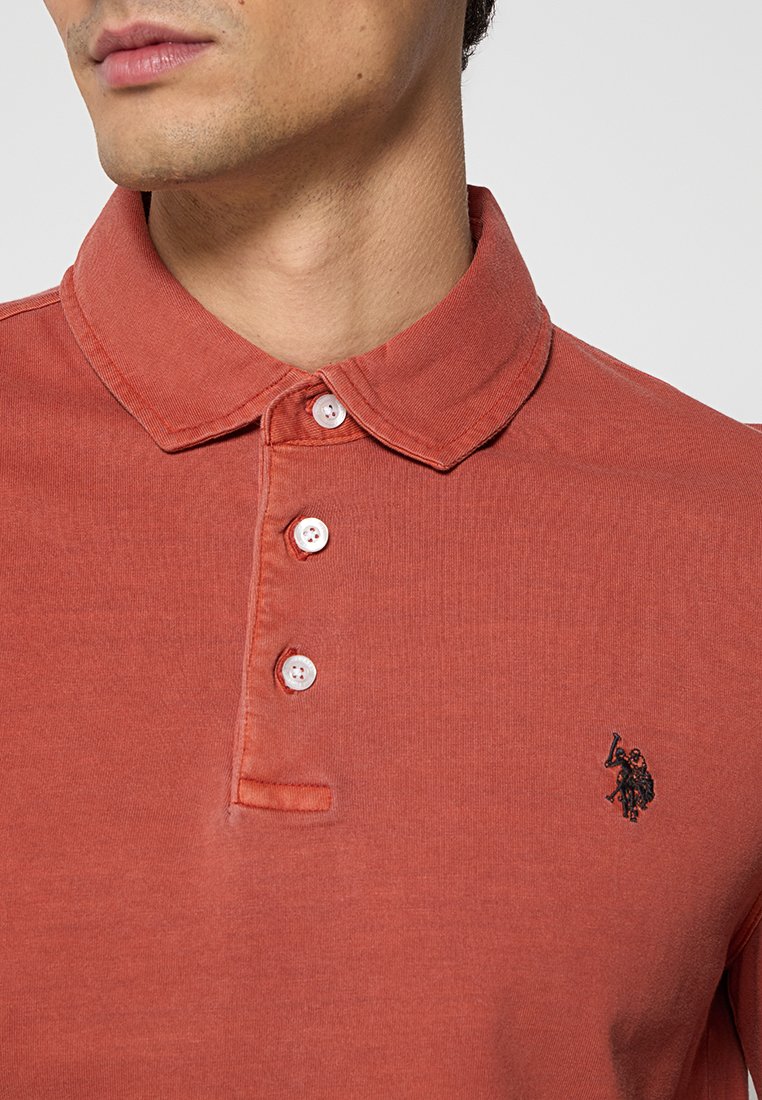 Einohrfarbenes Polo-Shirt aus weichem Stoff, mit einem klassischen Kragen, drei weißen Knöpfen und einem kleinen gestickten Logo auf der Brust.