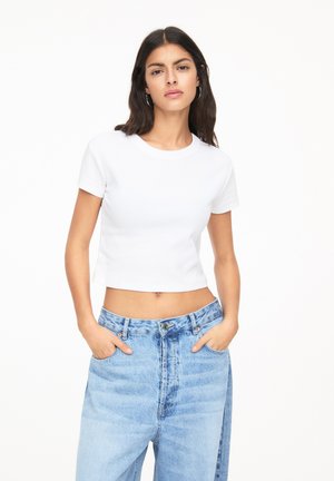 Crop top blanc à manches courtes avec un col rond, associé à un jean en denim taille haute bleu clair avec une texture délavée.