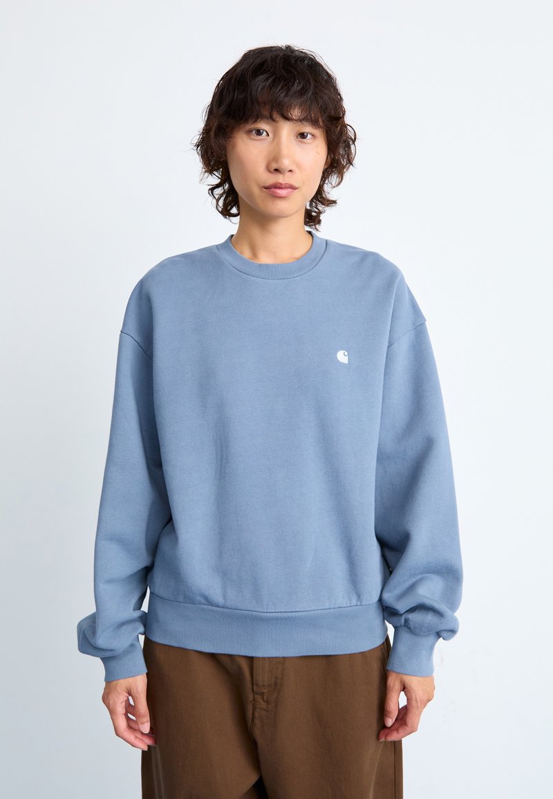 Light blue sweatshirt made of soft fabric, features a ribbed crew neck and cuffs, and a small white logo on the chest. Loose fit design.