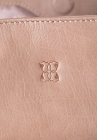 Light pink leather with a smooth texture, featuring a subtle embossed logo. Stitching detail along the edges adds structure.