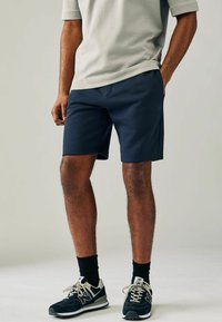 Bermudas azul marino en un material suave con un corte relajado, combinadas con una camiseta gris claro y deportivas negras con detalles grises.