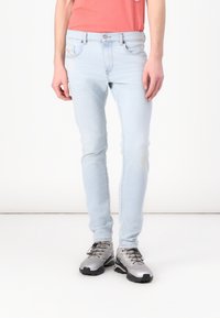 Jeans in denim azzurro chiaro con vestibilità slim, caratterizzati da dettagli sbiaditi, cinque tasche e chiusura con bottone, abbinati a scarpe da trekking grigie.