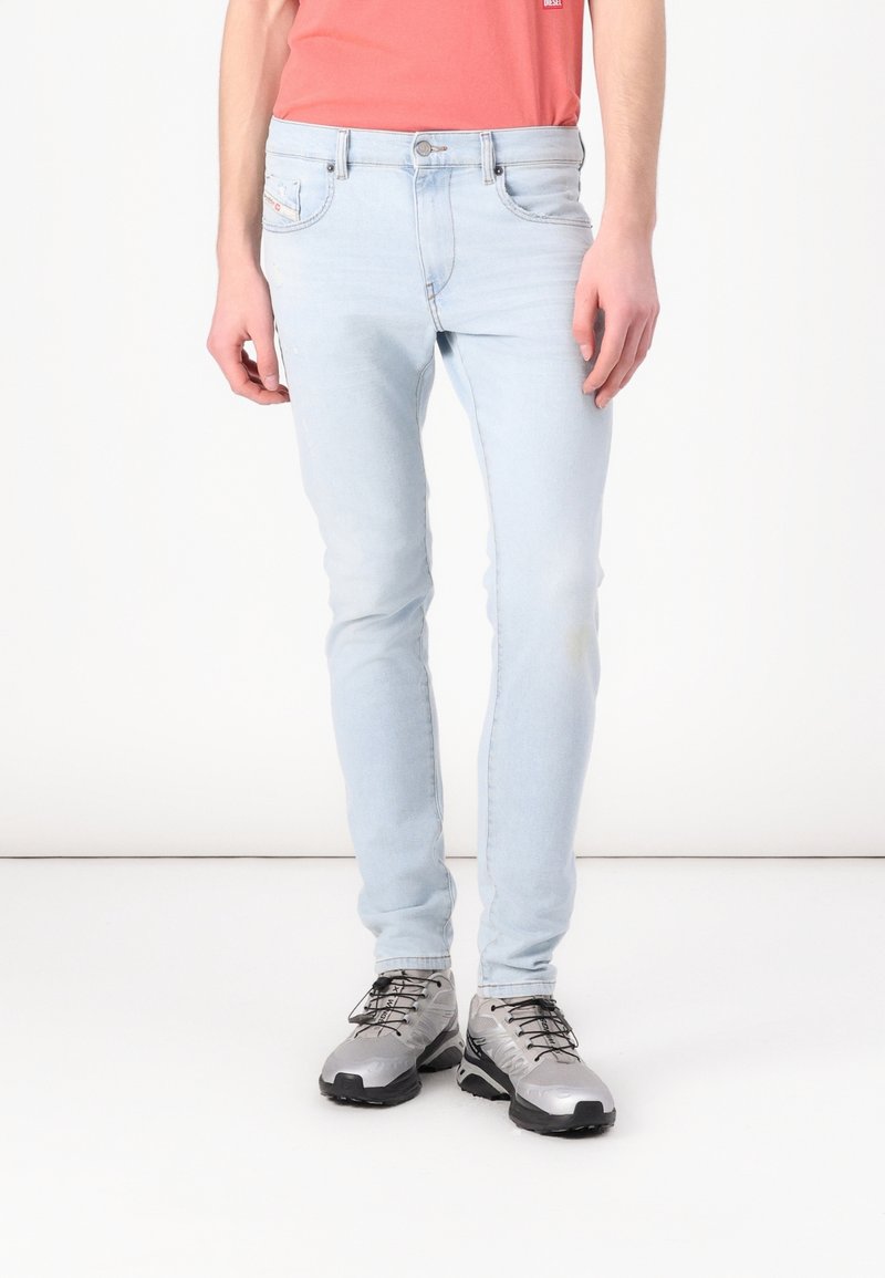 Jeans in denim azzurro chiaro con vestibilità slim, caratterizzati da dettagli sbiaditi, cinque tasche e chiusura con bottone, abbinati a scarpe da trekking grigie.