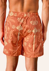 Herren Schwimmshorts in Koralle mit einem Muster aus tropischen Blättern und Sonne. Sie verfügen über einen elastischen Bund und eine leichte, glatte Textur.