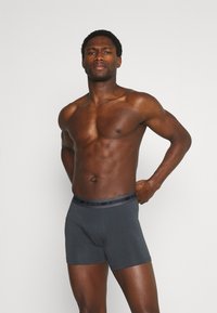 Shorts boxer grigi scuri realizzati in un tessuto morbido con un elastico nero in vita etichettato "JBS UNDERWEAR." Il modello si presenta con un'espressione neutra.