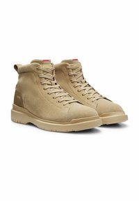 Paire de baskets montantes en daim beige avec lacets beiges, semelles en caoutchouc et un marquage subtil sur la languette et le talon.